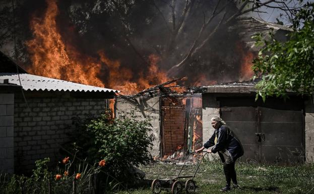A woman walks with the remains of a cart next to her burned house in Lisichans k, Donbas./AFP