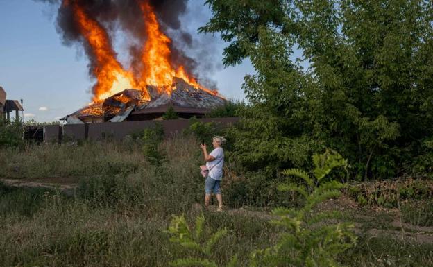 A woman takes a picture of a house that is burning after an attack.  /BULENT KILIC / AFP