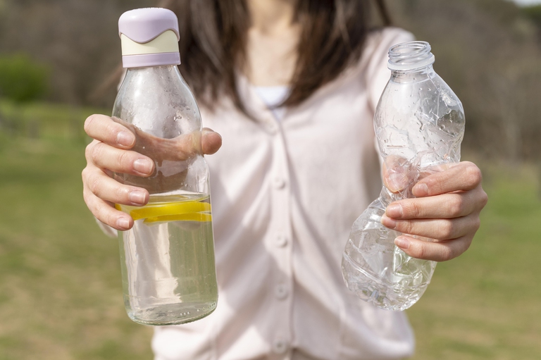 A woman holds a plastic bottle in one hand and a glass bottle in the other